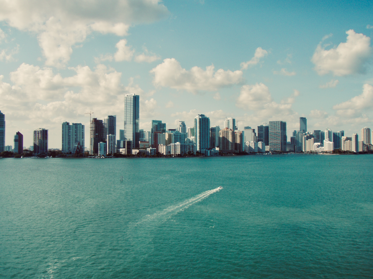 A stunning aerial view of Miami skyline with skyscrapers reflecting over blue waters under a clear sky.